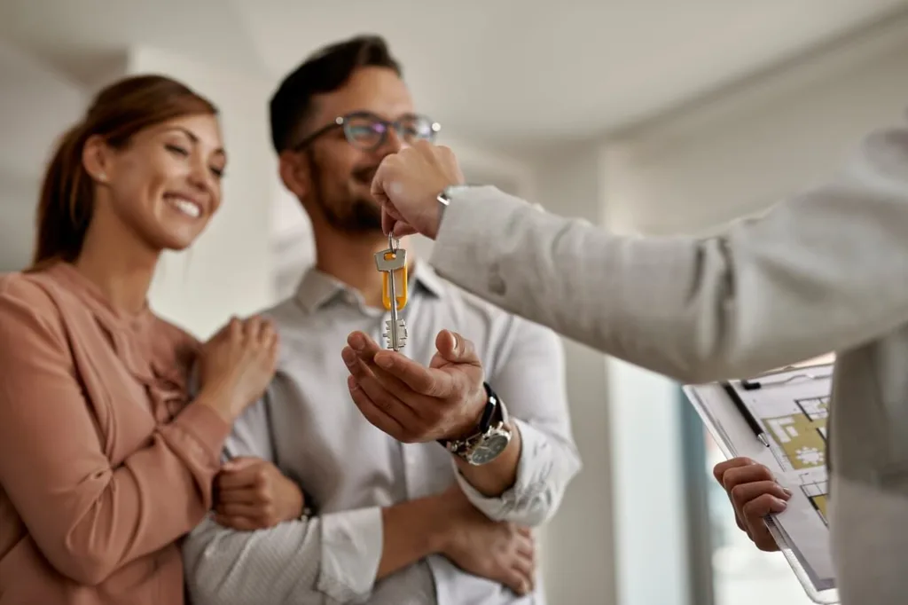 Sector inmobiliario Primer plano de un agente inmobiliario entregando las llaves de la nueva casa a una pareja